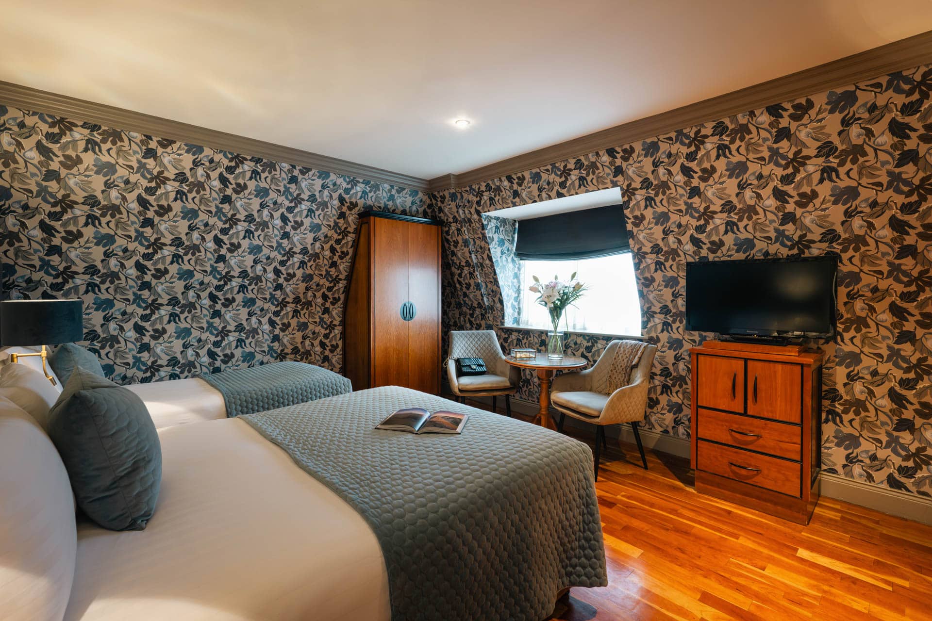 Superior room showing two beds, wooden flooring, seating area by window and television on chest of drawers.