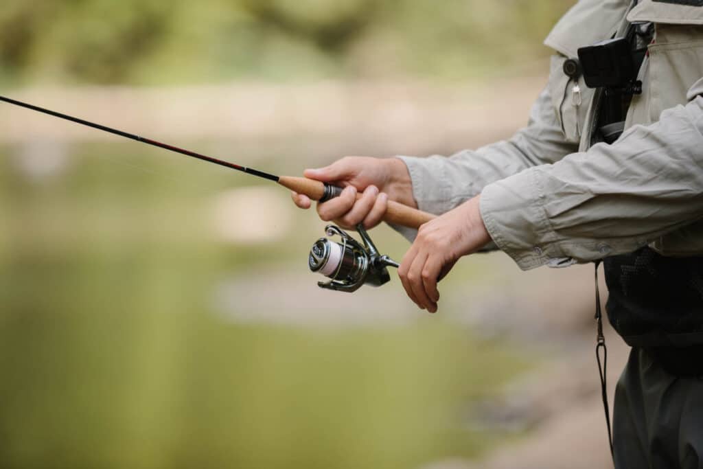 Fisherman holding a fishing rod, in a serene river surrounded by nature's beauty