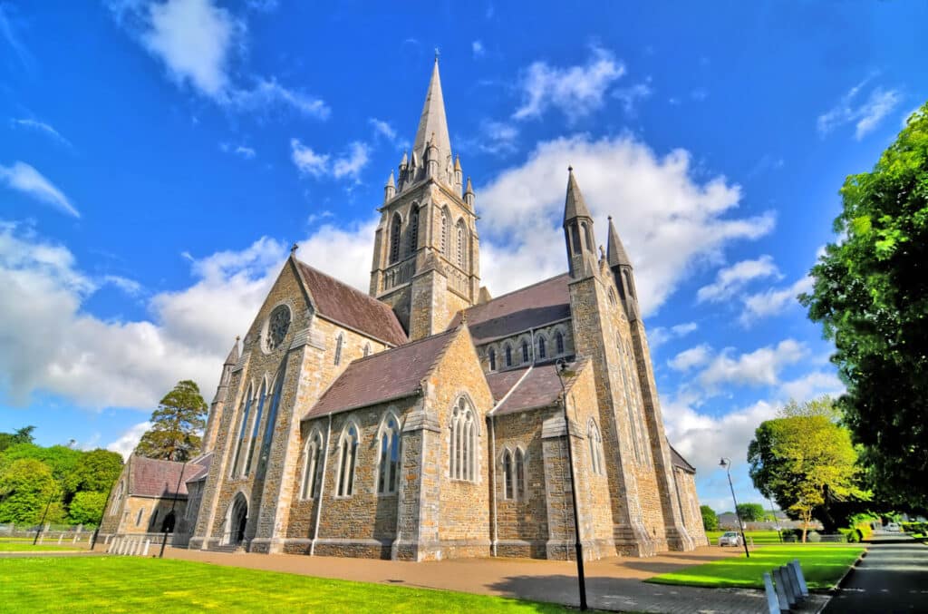 St Mary’s Cathedral in Killarney, a Gothic style stone cathedral set within green parkland under a bright blue sky.